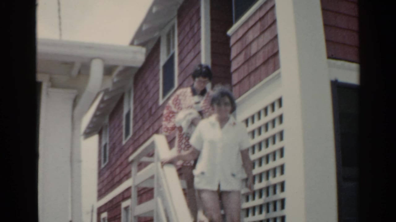 In 1959 San Francisco home-movie footage, two women come down white stairs outside a red-shingled house with white trim.