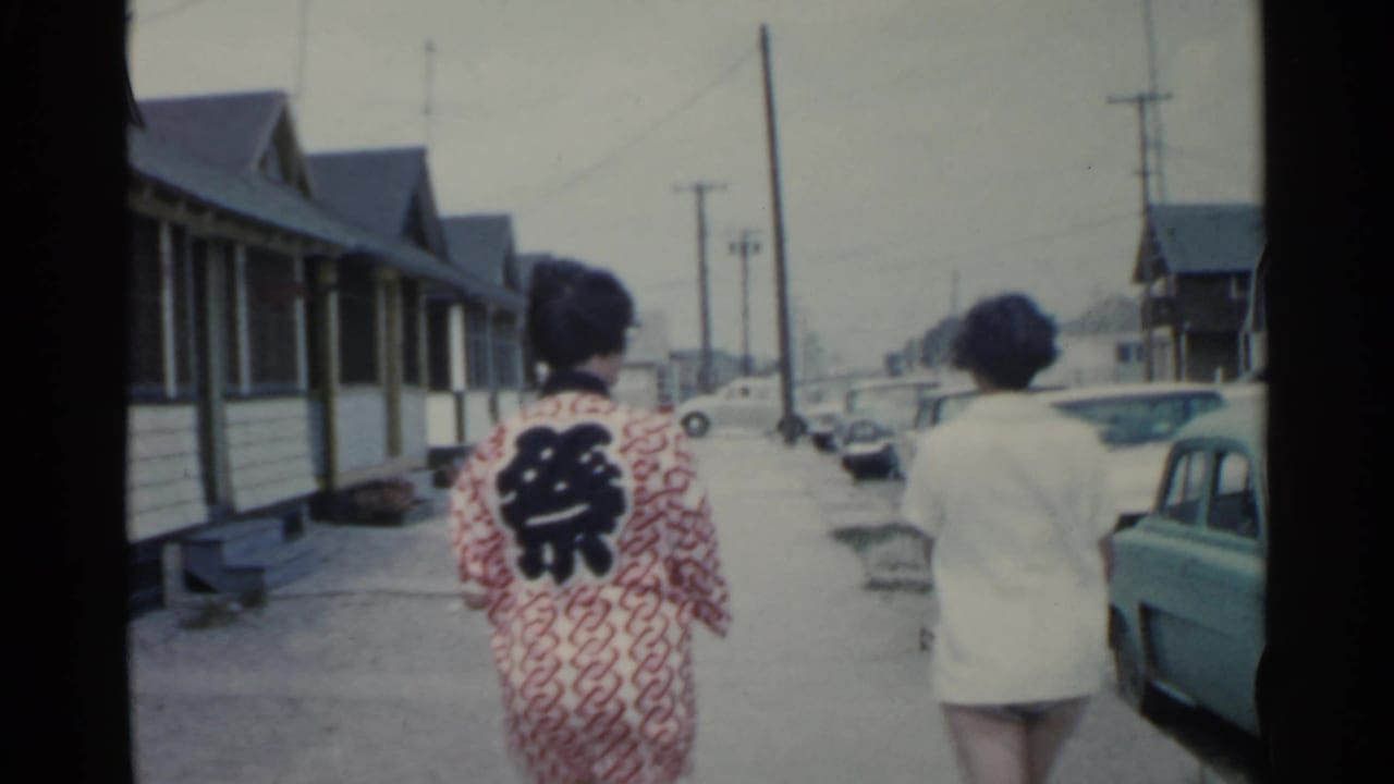 The pair continues walking away from the camera on a 1959 San Francisco residential street with vintage cars along the curb.