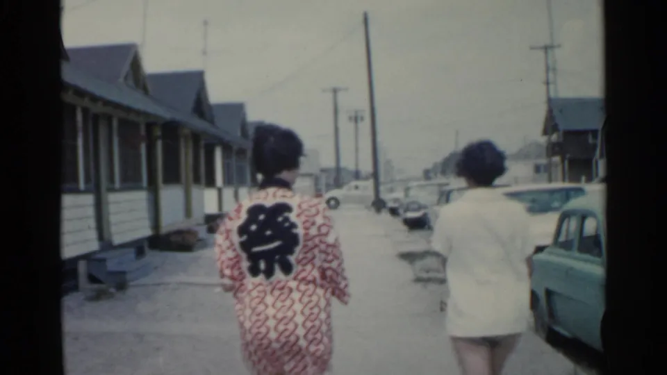 The pair continues walking away from the camera on a 1959 San Francisco residential street with vintage cars along the curb.