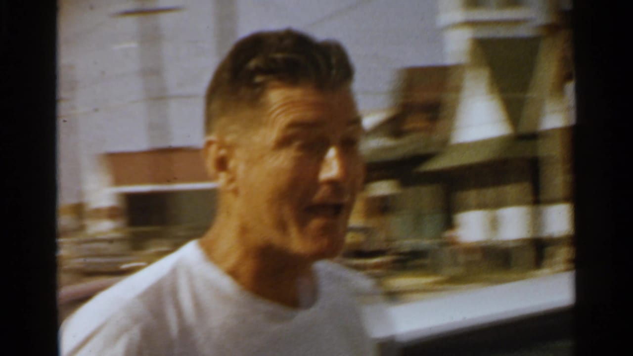 A man in profile moves past a white vintage car on a 1959 San Francisco residential street.