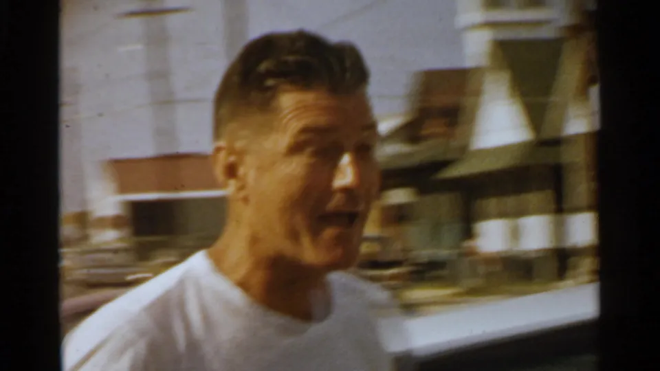A man in profile moves past a white vintage car on a 1959 San Francisco residential street.
