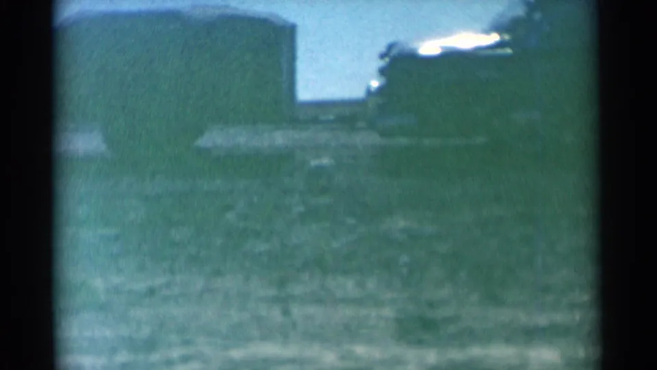 A small dog appears low in the 1959 South Dakota field as the parked vehicle and light structure remain in the background.