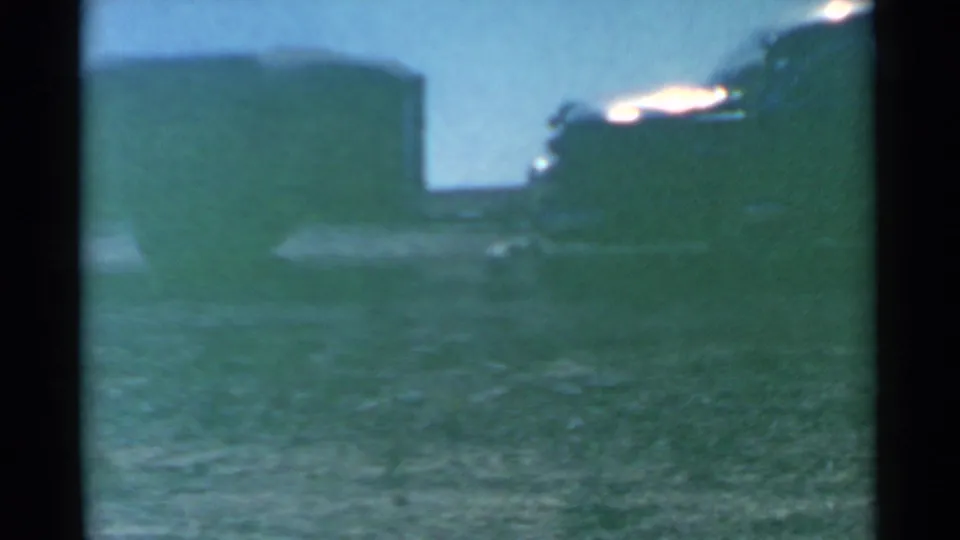1959 South Dakota 8mm frame showing a dark parked vehicle beside a flat grassy field, softened by grain and color shift.