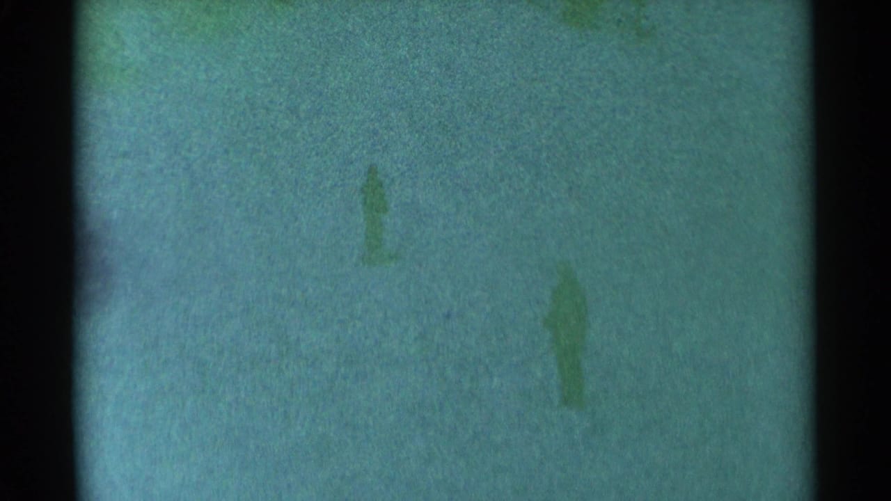 1959 South Dakota 8mm frame showing a tiny indistinct figure on a green-tinted snowy hillside.