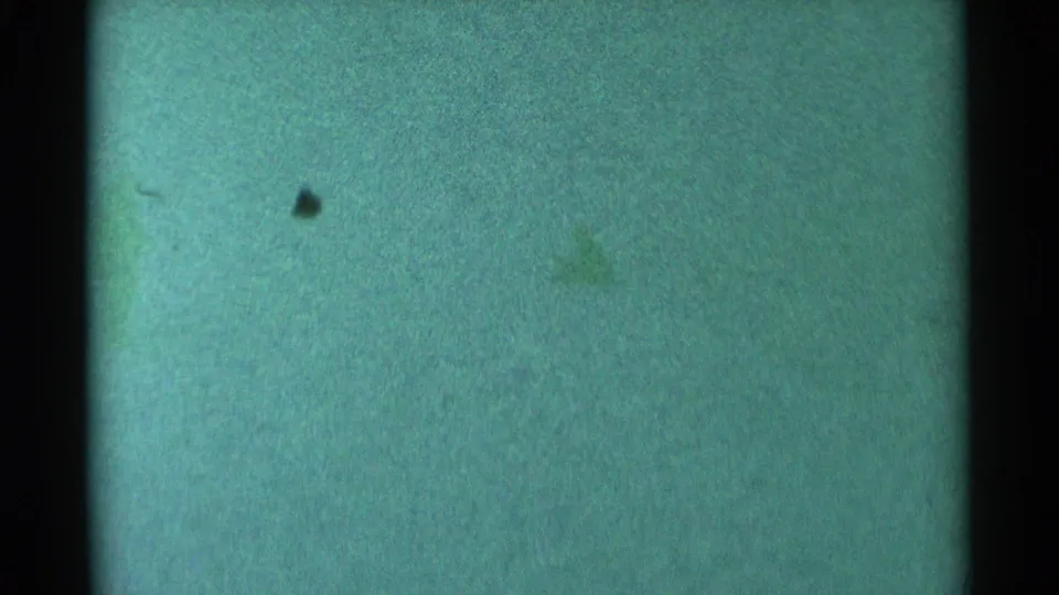 Indistinct dark silhouette on a green-tinted snowy South Dakota hillside, scanned from 1959 8mm home-movie film.