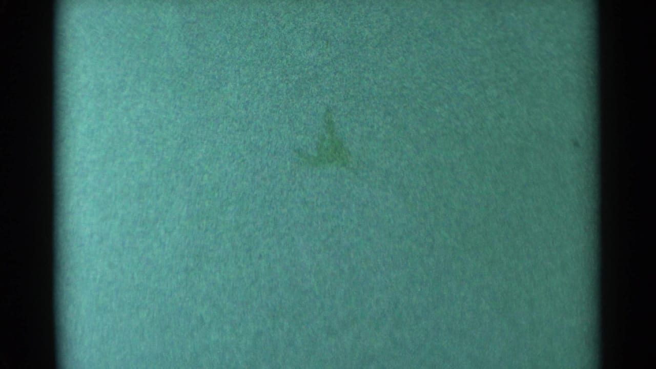 1959 South Dakota 8mm frame showing green-blue tint, dark film edges, grain, dust, and an obscuring horizontal band.