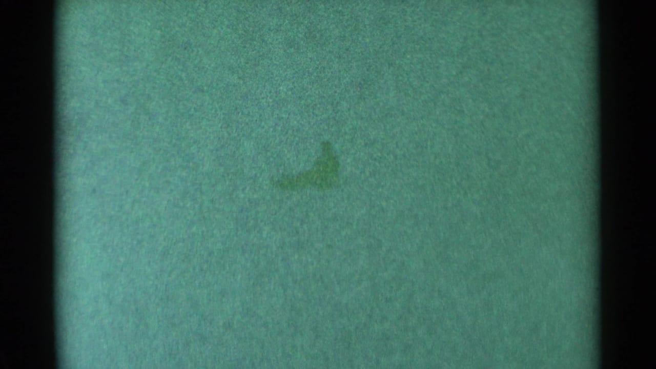 1959 South Dakota 8mm frame showing a distant, indistinct dark sledding form on a green-tinted snowy hill.