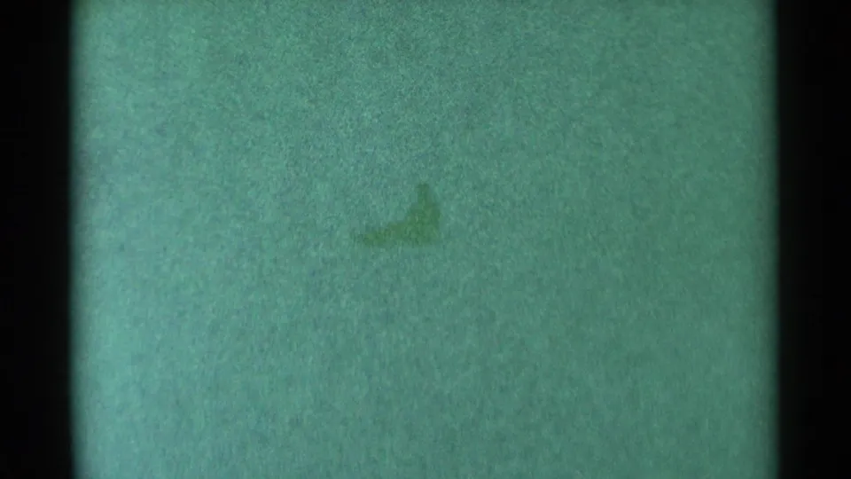 1959 South Dakota 8mm frame showing a distant, indistinct dark sledding form on a green-tinted snowy hill.
