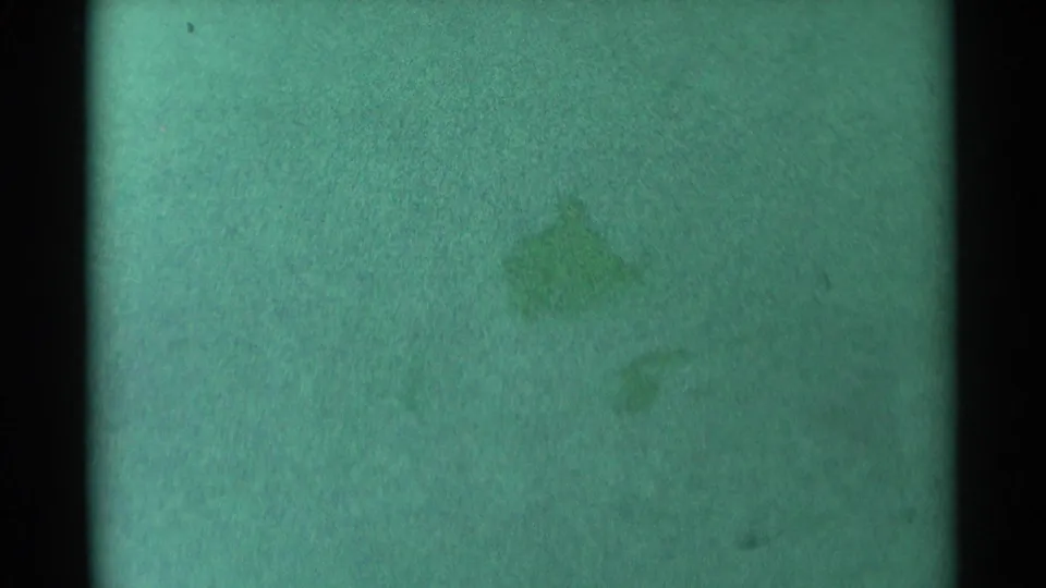 Green-tinted 8mm frame from South Dakota with a faint sledding form near the lower right of the snowy hill.