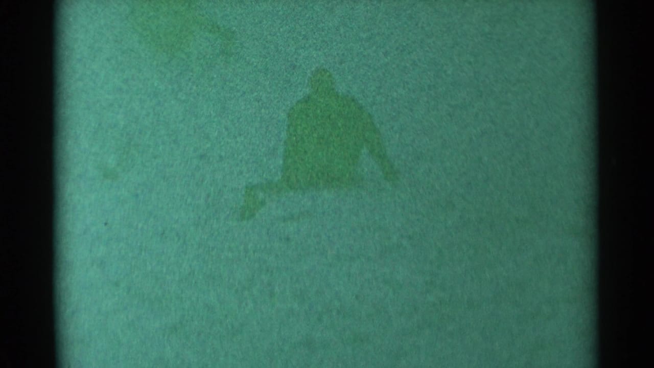 Sledder partly upright on a snowy slope, seen through heavy grain and tint.