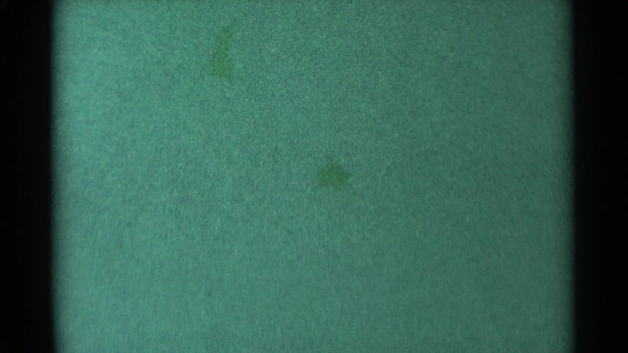 Green damaged film frame with water texture, scratches, and a dark vertical frame bar.