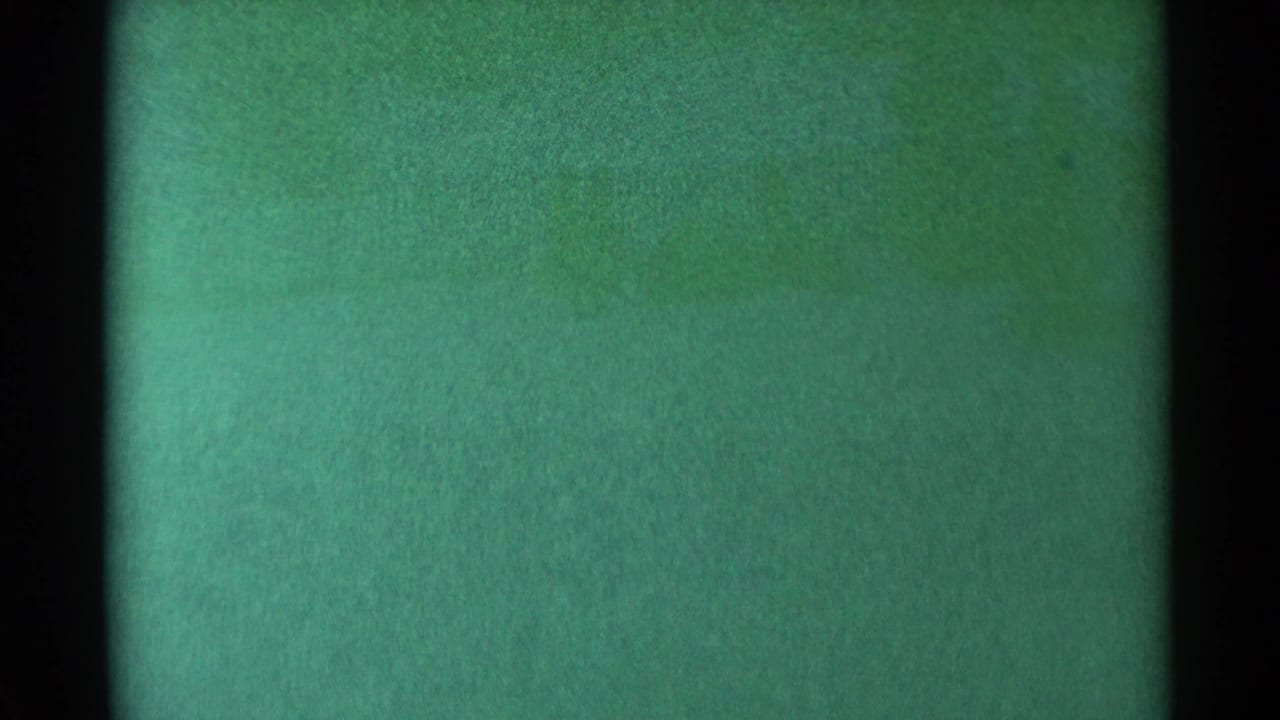 Green-tinted grainy 8mm frame with dark vertical borders and no distinct subject visible.