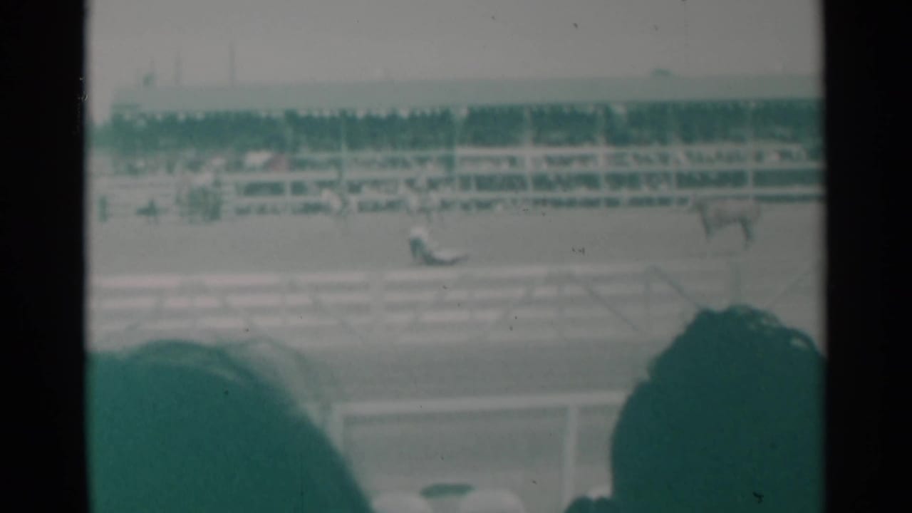 1960 Cheyenne rodeo view from the crowd, showing horses in the arena and filled grandstands beyond the rail.