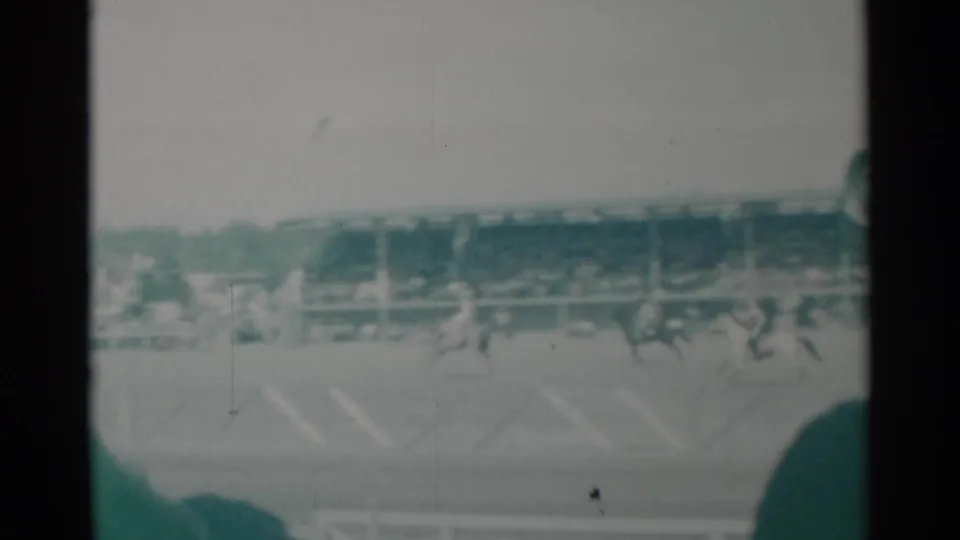 1960 Cheyenne rodeo view with bronco riders crossing the arena before crowded grandstands in soft green-tinted 8mm footage.