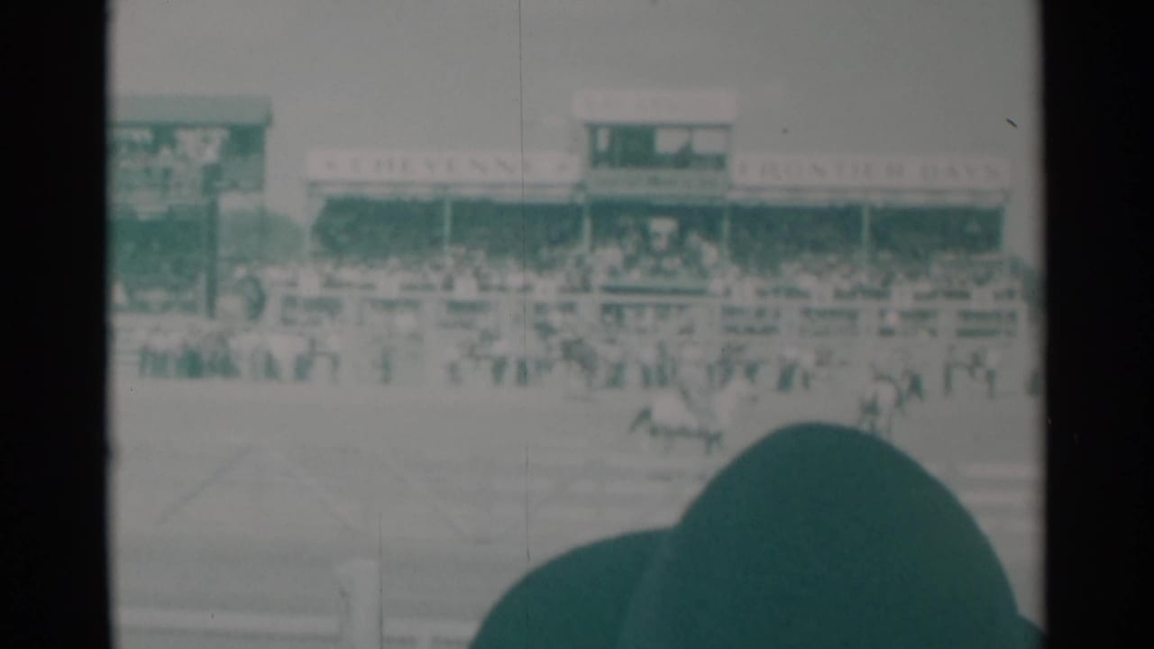 At the Cheyenne rodeo, a horse and rider move across the arena while the grandstand and Frontier Days signage remain visible behind them.