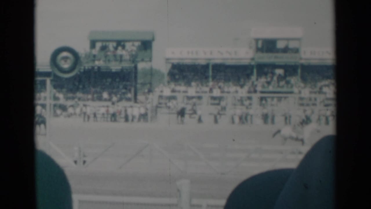 1960 Cheyenne, Wyoming 8mm frame showing riders on horses racing past grandstands with spectators and Frontier Days signage.