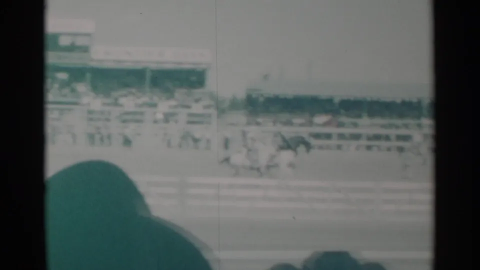 1960 Cheyenne, Wyoming home-movie frame showing a dark horse and rider racing past the rail with spectators behind.