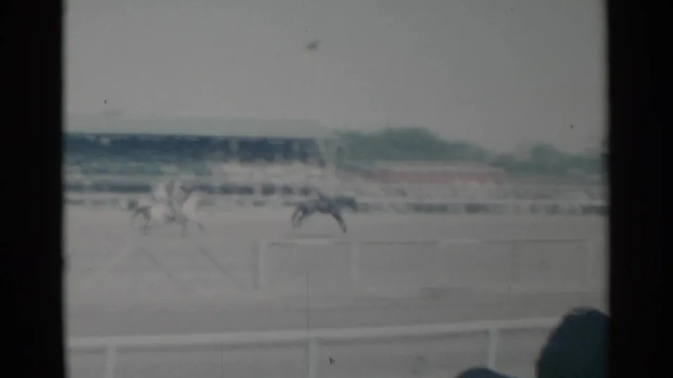 1960 Cheyenne Frontier Days horse race viewed from the stands, with riders on the track and a distant crowd behind the rail.