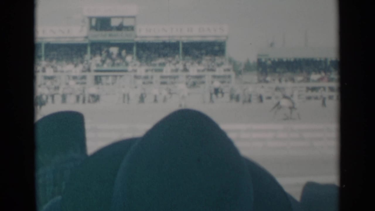 Grandstand and track seen past dark foreground spectator silhouettes as a rider passes at right.