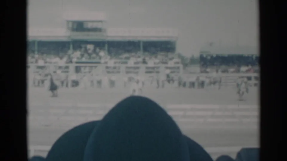 Cheyenne Frontier Days track view with grandstands and rail fencing, filmed from behind spectators during the horse race.
