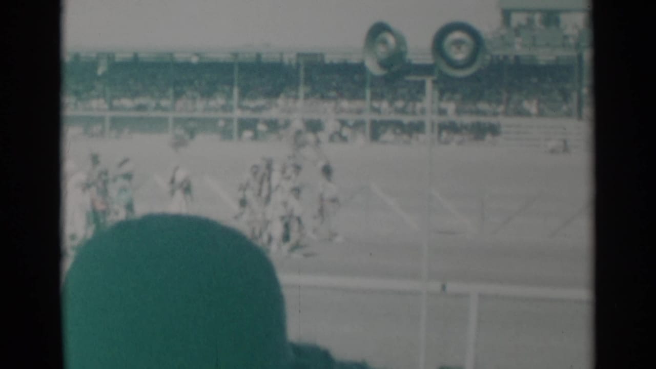 Riders and horses appear near the Cheyenne racecourse while a seated crowd watches from the grandstand in 1960 home-movie footage.