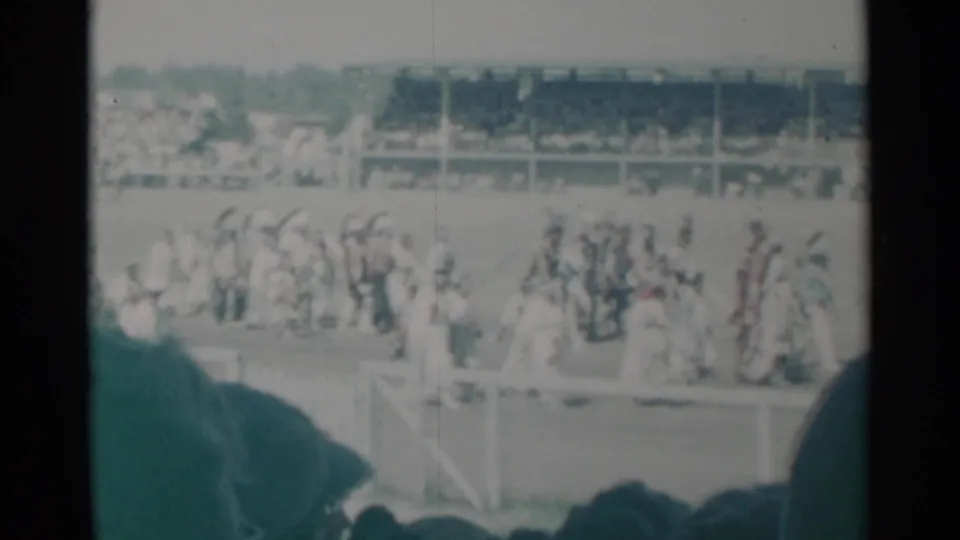Cheyenne horse race scene with riders and horses near the rail, spectators in the grandstand, and dark foreground silhouettes from the stands.