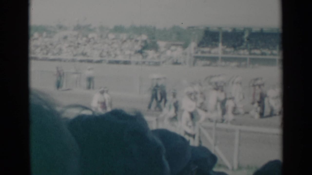 Crowds and small groups move across a Cheyenne event field, with stands full of spectators in the background.