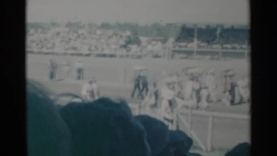 Crowds and small groups move across a Cheyenne event field, with stands full of spectators in the background.