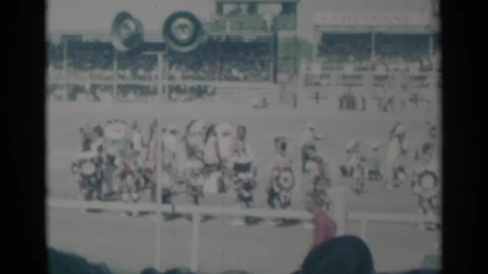 Cheyenne event participants gather across the field, framed by spectator silhouettes and crowded grandstands.