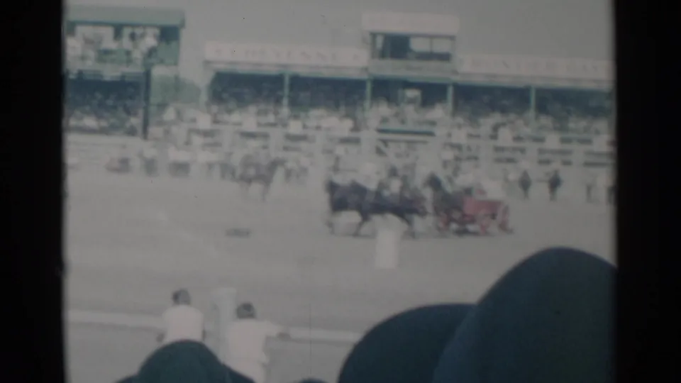 Cheyenne Frontier Days arena scene with chariot teams racing before a crowded grandstand, filmed from a home-movie spectator angle.