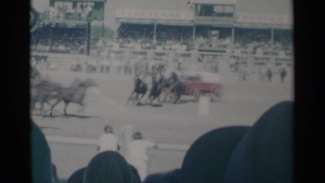 In Cheyenne, Wyoming, 1960 home-movie footage, a horse team appears to pull a red cart past spectators at a rodeo or fairground track.