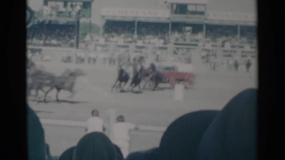 In Cheyenne, Wyoming, 1960 home-movie footage, a horse team appears to pull a red cart past spectators at a rodeo or fairground track.