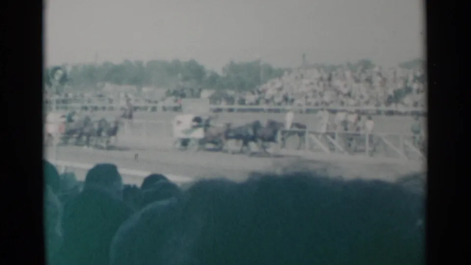 A wide spectator view in Cheyenne shows grandstand crowds watching horse-drawn racing near the track rail in 1960 home-movie footage.