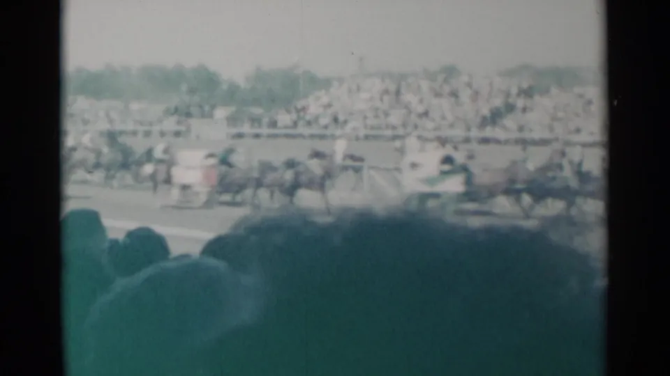 1960 Cheyenne, Wyoming home-movie view of horses racing past crowded grandstands, partly obscured by audience silhouettes.