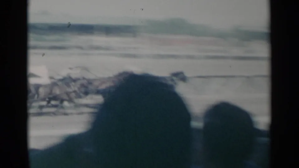 1960 home-movie frame of racehorses in motion at the track, heavily blurred by speed and handheld filming from the crowd.