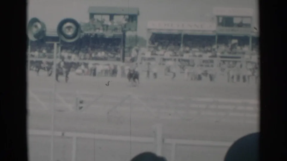1960 home-movie view in Cheyenne, Wyoming, showing riders on horseback near a track with grandstands and event signage behind them.