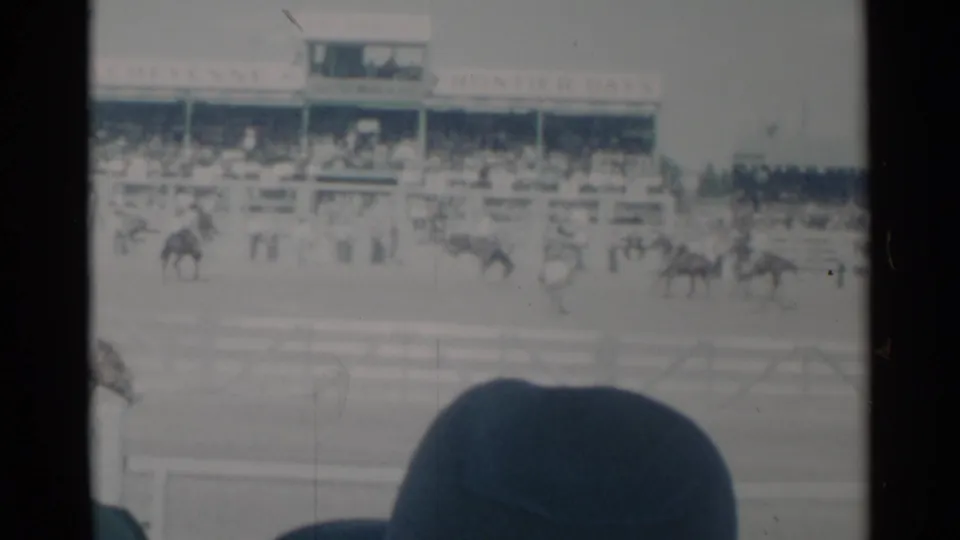 1960 Cheyenne, Wyoming home-movie frame with horses and riders moving across the track before packed grandstands and visible event signage.