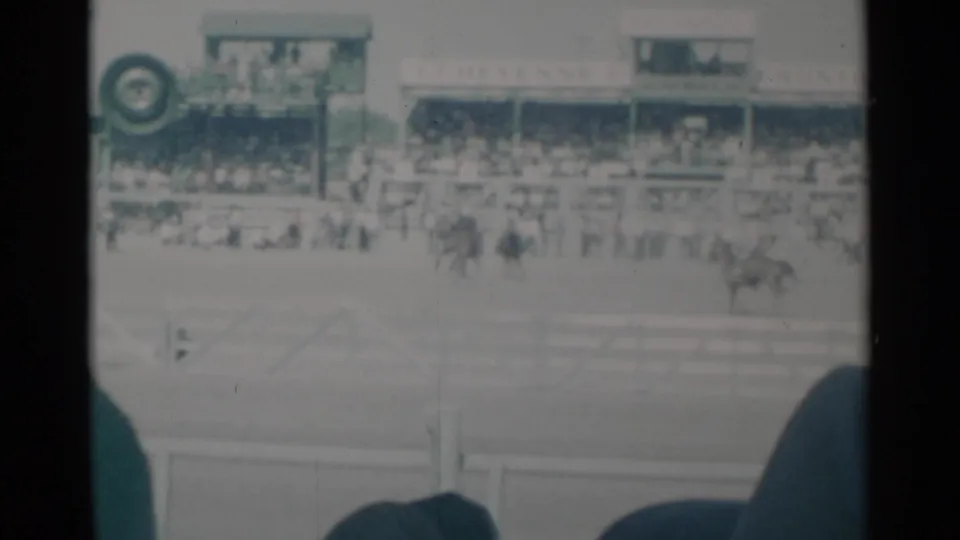 Cheyenne Frontier Days rodeo arena with a distant rider, crowd-filled stands, and visible event signage above the spectators.