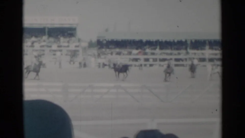 Cheyenne Frontier Days rodeo arena scene with several riders, horses, rail fencing, and a spectator hat partly blocking the lower frame.