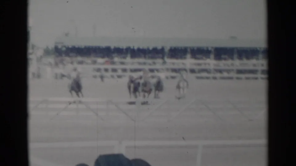 1960 Cheyenne rodeo footage showing riders and horses grouped in the arena, with spectators and fencing visible behind them.