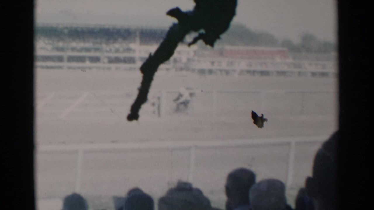 Distant rodeo action in an arena with spectators below and a dark obstruction near the lens.