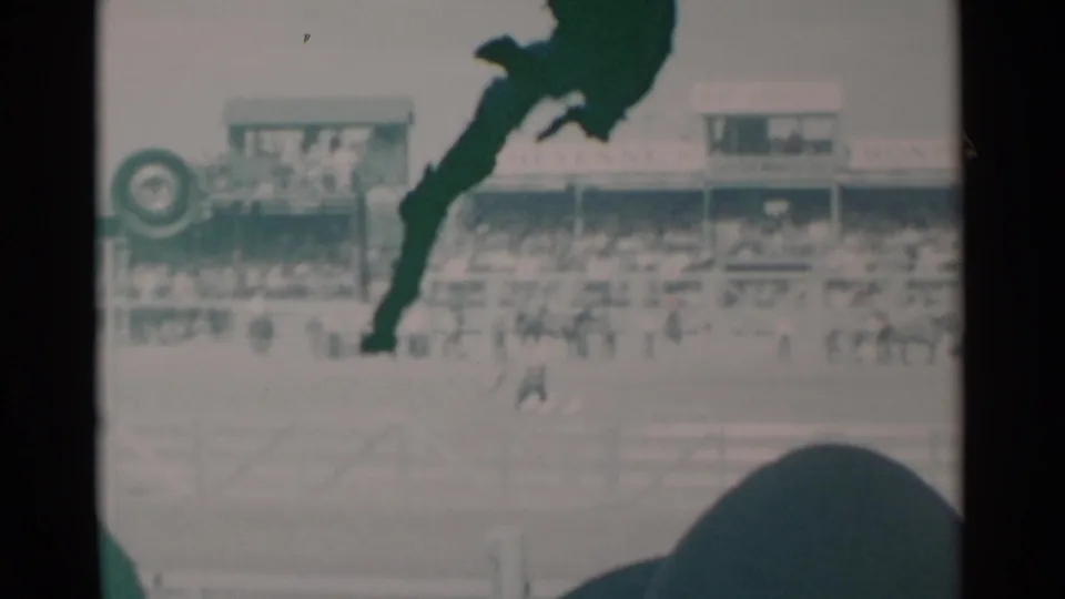 1960 Cheyenne rodeo arena with a distant handler, dog and ducks on the arena floor, spectators in stands, and a visible circular sign.