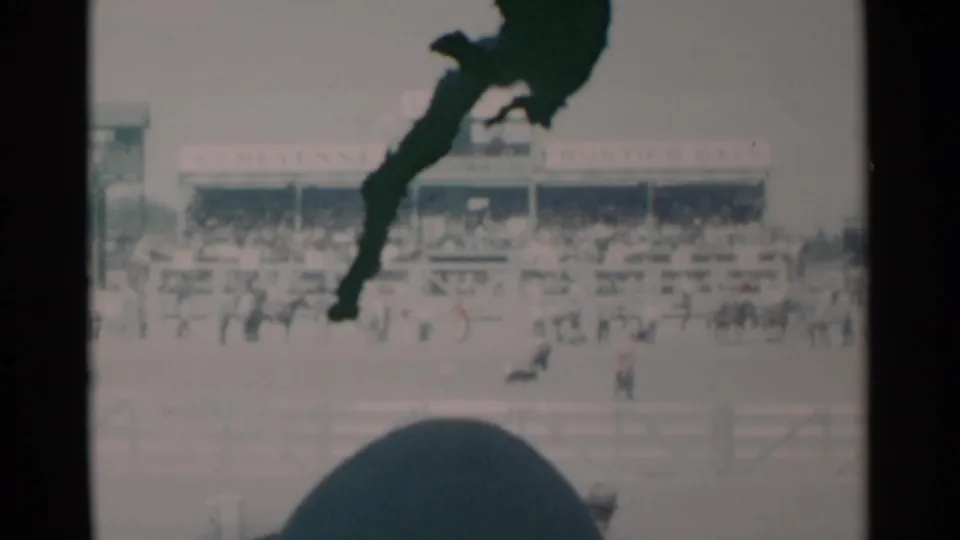 1960 Cheyenne rodeo grounds with spectators in the stands, arena figures, and a dark foreground shape partly blocking the 8mm frame.