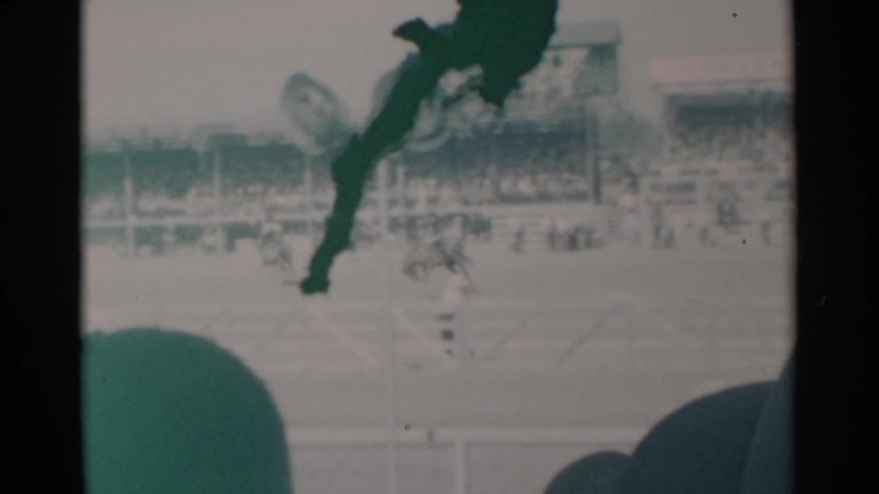 Home-movie frame from Cheyenne, Wyoming, showing rodeo action in front of crowded grandstands and foreground viewers.