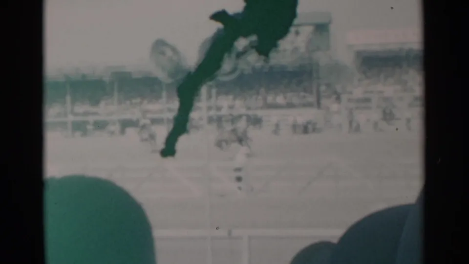 Home-movie frame from Cheyenne, Wyoming, showing rodeo action in front of crowded grandstands and foreground viewers.