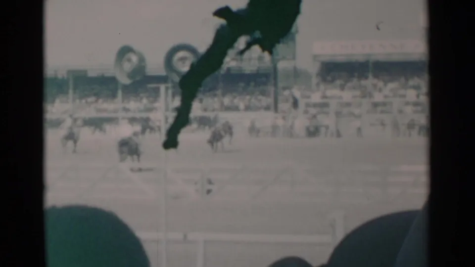 Visitor-shot 8mm frame from a 1960 Cheyenne rodeo, with bronco action in the arena and spectators in the background.