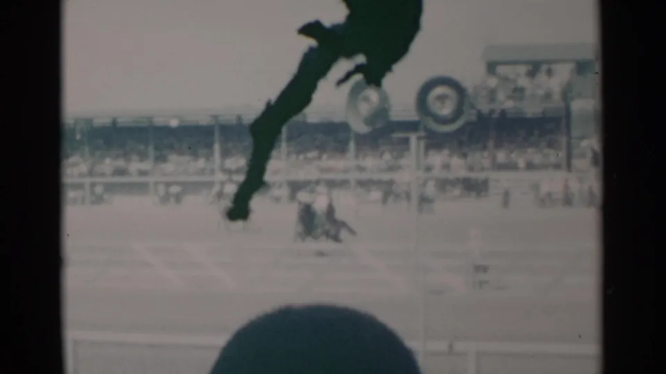 1960 Cheyenne rodeo frame showing bronco riding action from the stands, with spectators, signage, and a foreground silhouette.