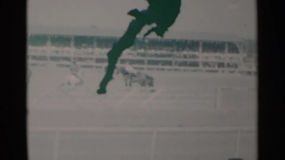 A 1960 Cheyenne arena horse race appears in soft 8mm color, with riders in the distance and a dark foreground object obscuring part of the frame.