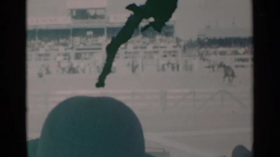 1960 Cheyenne home-movie view of a horse race, with a large spectator hat in the foreground and crowded bleachers behind the arena.