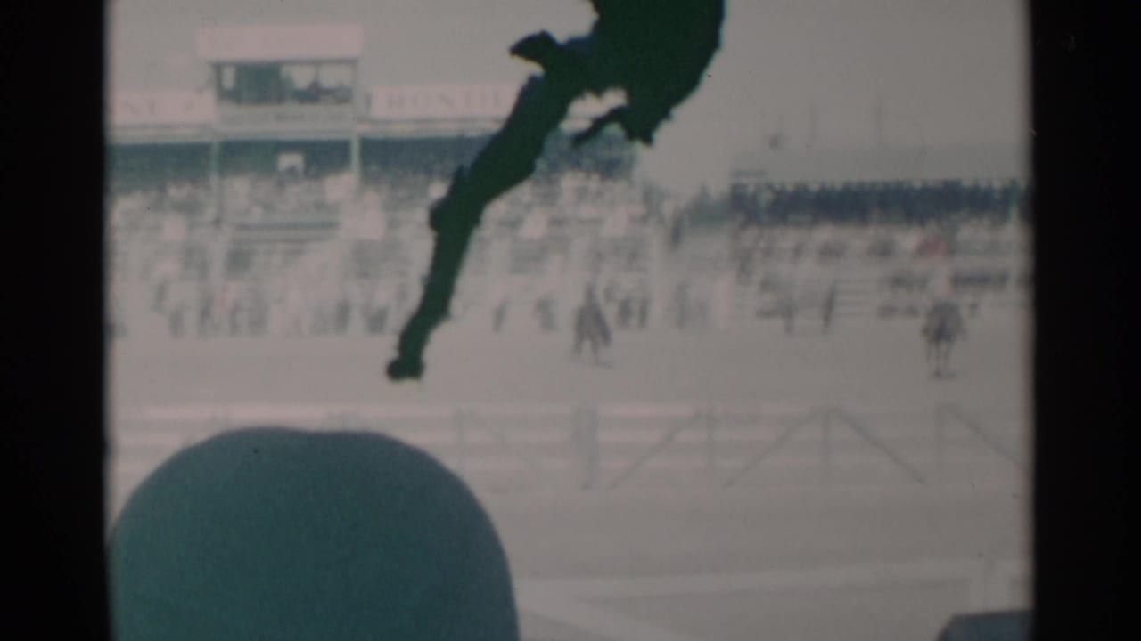 1960 Cheyenne rodeo scene with riders in the arena, spectators in the stands, and a dark green film artifact over the frame.